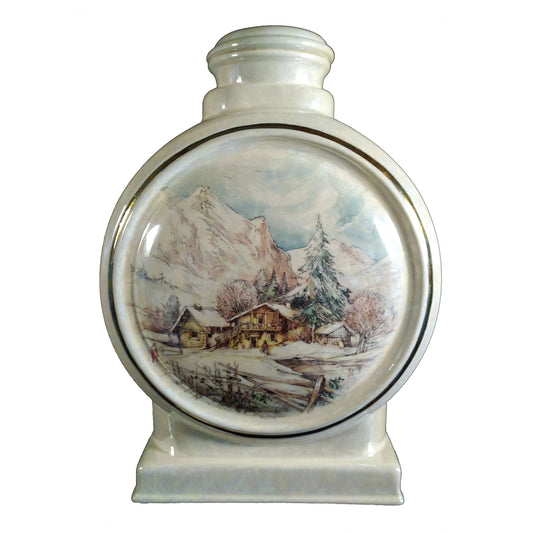 A beautiful large sized cremation ceramic urn with a decoration of a wintery scene of a home or chalet and mountain with a gold highlight mother-of-pearl finish.