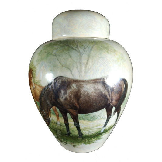 A beautiful medium sized cremation ceramic urn with a decoration of a scene of two horses grazing with a mother-of-pearl finish.