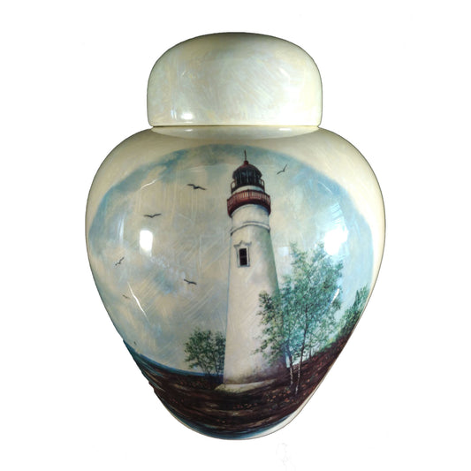 A beautiful medium sized cremation ceramic urn with a decoration of a scene of a white Lighthouse on a rocky coastline with a mother-of-pearl finish.