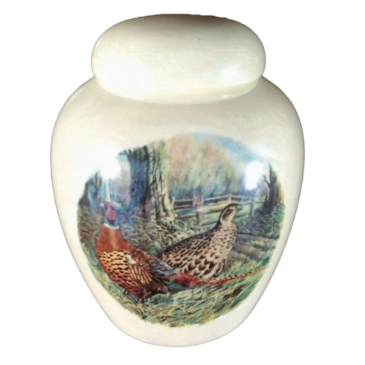 A beautiful small-sized cremation ceramic keepsake urn with a decoration of a pair of pheasants in a fall treed setting with a mother-of-pearl finish.