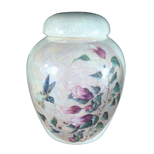 A beautiful small-sized cremation ceramic keepsake urn with a decoration of a hummingbird and a flower bush with a mother-of-pearl finish.