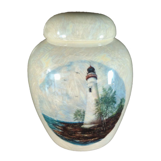 A beautiful small-sized cremation ceramic keepsake urn with a decoration of a lighthouse on a rocky shoreline with a mother-of-pearl finish.