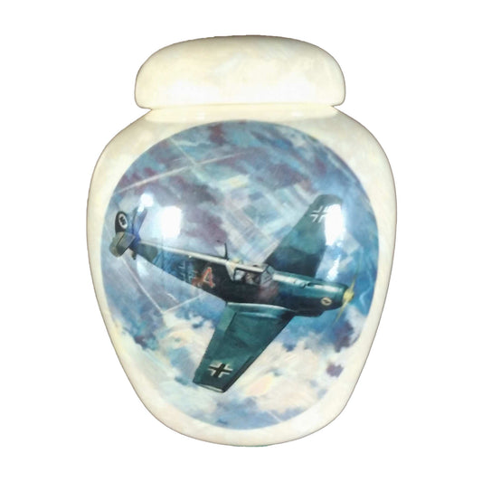 A beautiful small-sized cremation ceramic keepsake urn with a decoration of a green airplane with German markings flying over farm fields with a mother-of-pearl finish.