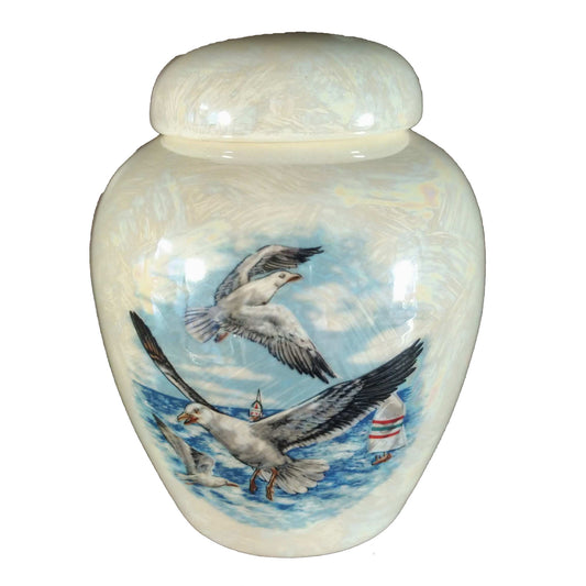 A beautiful small-sized cremation ceramic keepsake urn with a decoration of a group of seagulls flying over water and bouys with a mother-of-pearl finish.