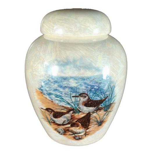 A beautiful small-sized cremation ceramic keepsake urn with a decoration of a group of terns on the shore near a body of water with a mother-of-pearl finish.