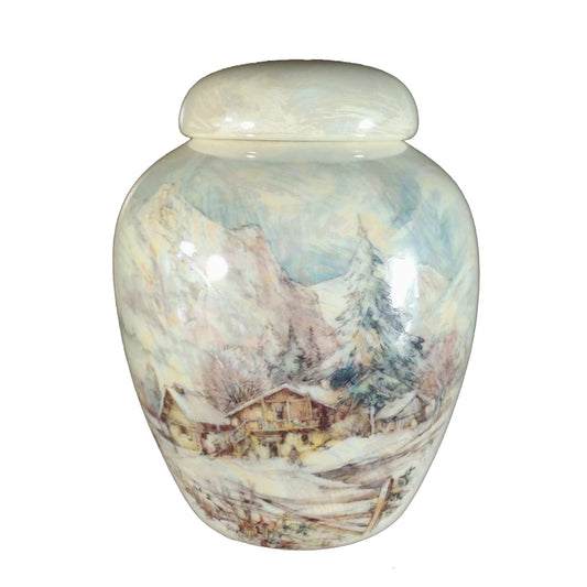 A beautiful small-sized cremation ceramic keepsake urn with a decoration of a wintery scene of a home or chalet and mountain with a mother-of-pearl finish.