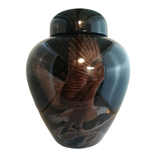 A beautiful medium sized cremation ceramic urn with a decoration of a bald eagle taking flight from a tree limb with a gloss black finish.