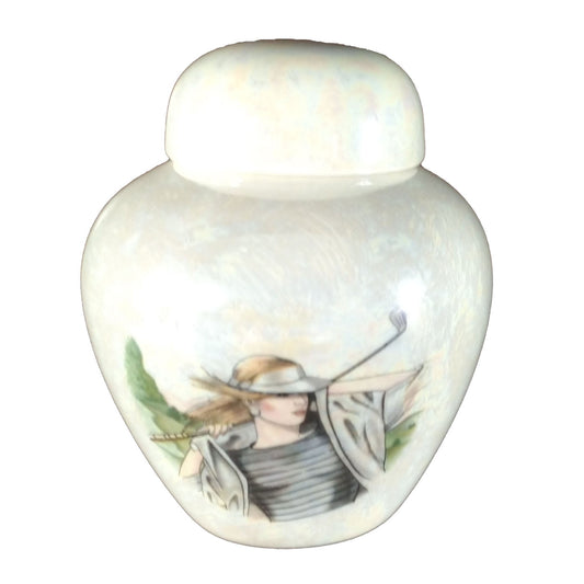 A beautiful small sized cremation ceramic keepsake urn with a decoration of a lady golfer with a mother-of-pearl finish.