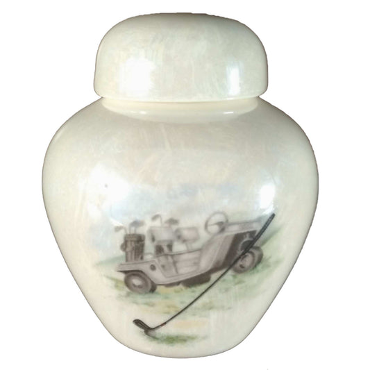 A beautiful keepsake cremation ceramic keepsake urn with a decoration of a golf cart sitting on golf course and a golf club and ball in front with a mother-of-pearl finish.