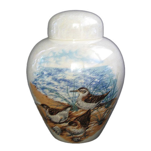 A beautiful medium sized cremation ceramic urn with a decoration of a scene of a group of terns on a seashore with a mother-of-pearl finish.